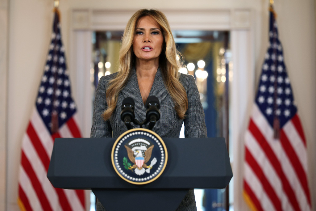 Melania Trump szürke kosztümben beszédet mond a kamerák előtt a Fehér Házban