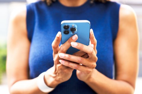 Egy kék ruhás nő egy kék mobiltelefont tart a kezeiben