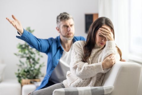 Egy férfi veszekedik a kanapén ülve egy nővel, aki a fejét fogja és ki van borulva