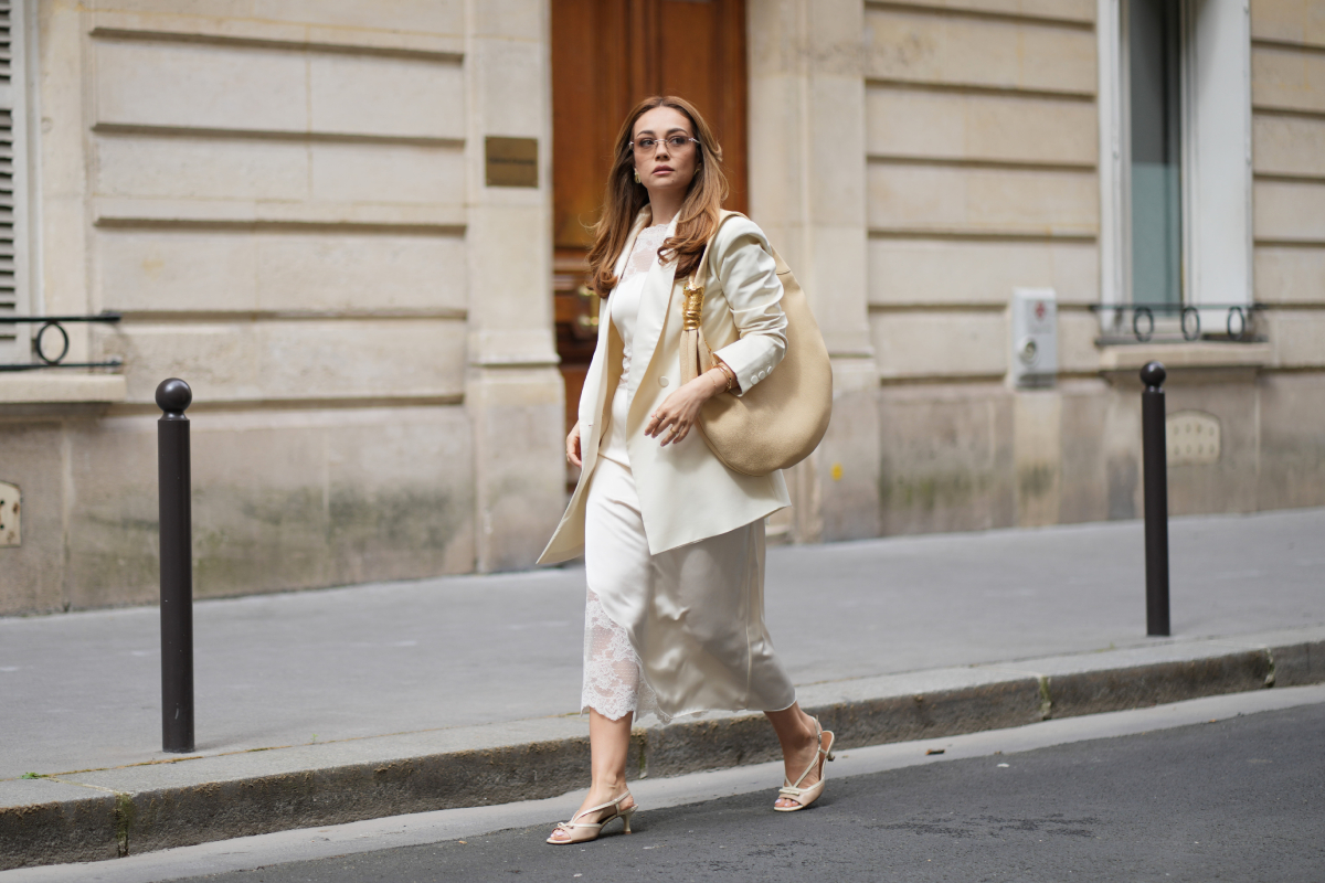 Merve Gorgoz hosszú, hullámos, világosbarna, középen elválasztott hajat visel, natúr sminket határozott szemöldökkel és nude rúzzsal, keret nélküli Tiffany & Co. napszemüveget, törtfehér The Frankie Shop oversized blézert bevágott hajtókával egy krémfehér Malina midiruha fölött, amelynek a felsőrészén és az alján csipke berakás található, arany ékszereket, egy bézs Schiaparelli nagyméretű bőr válltáskát arany szem díszítéssel, valamint bézs Parallele pántos magas sarkú cipőt