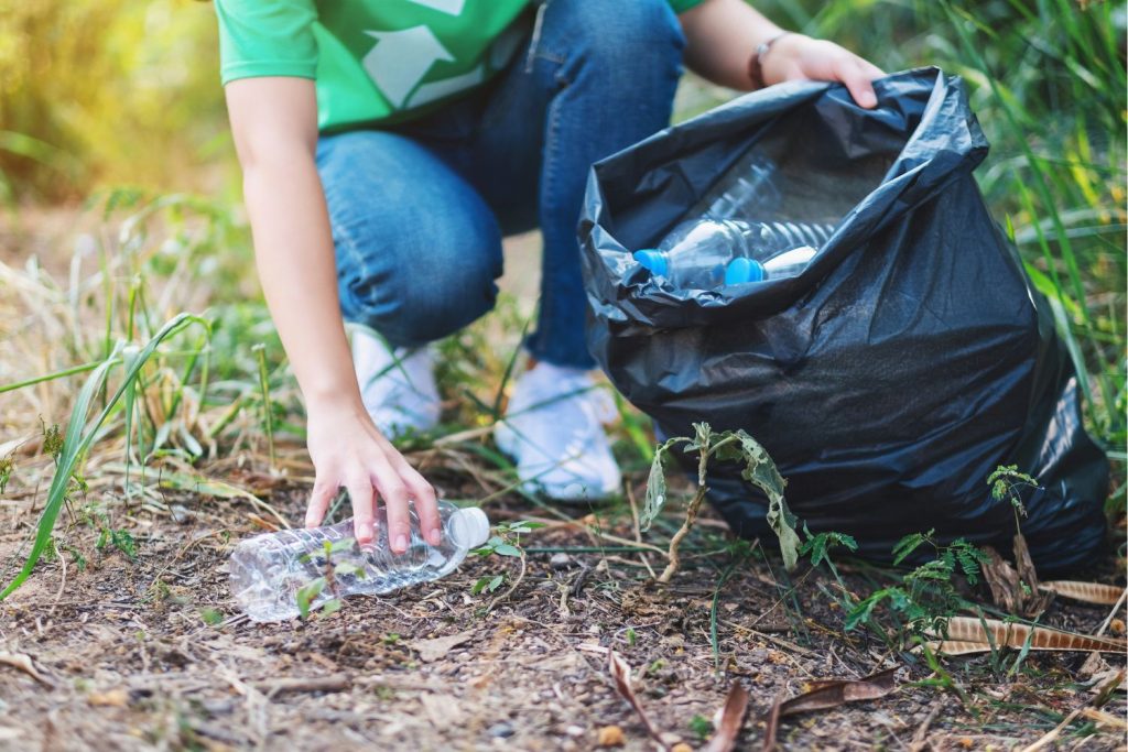 Szemétszedés Föld napján, nő fekete szemetesszákba erdő szélén műanyag palackot szed össze