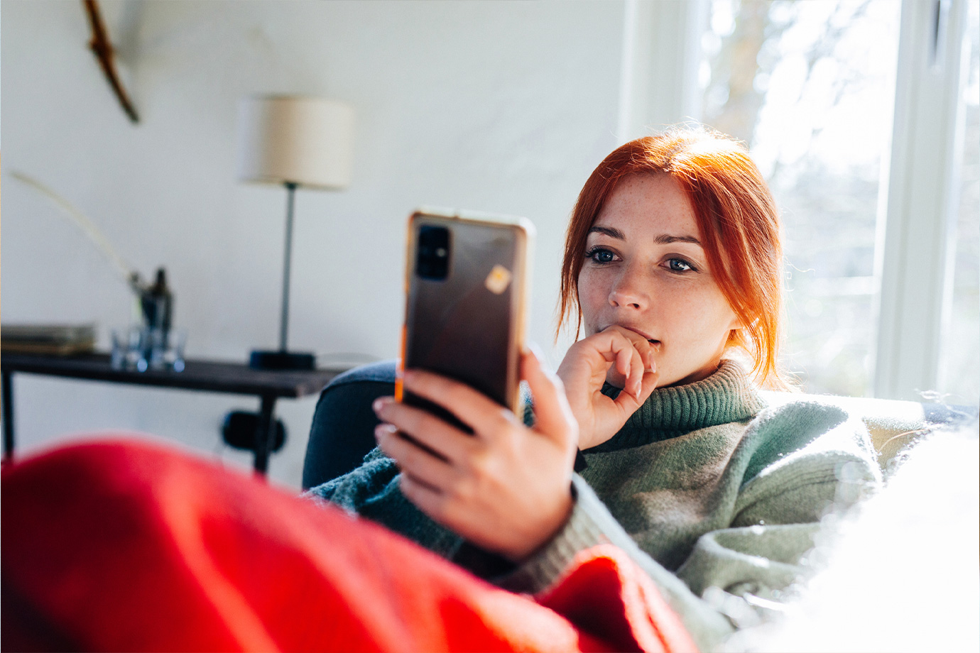 Vörös hajú nő nézi a mobiltelefonja képernyőjét