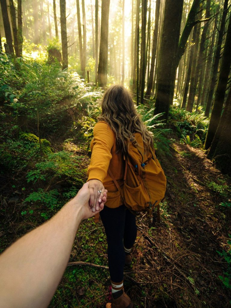 Túrázó pár erdőben, nő megy elől és hátranyújtja a kezét a férfinak