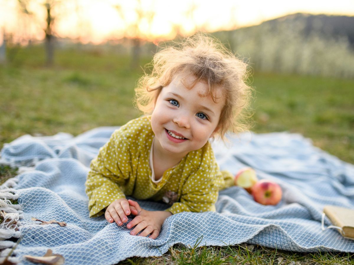 Vidáman mosolygó lány kisbaba hasal réten kék takarón