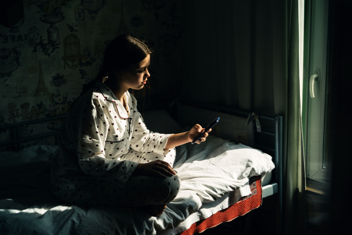 fiatal lány pizsamában ágyban ül és a telefonja kijelzőjét nézi