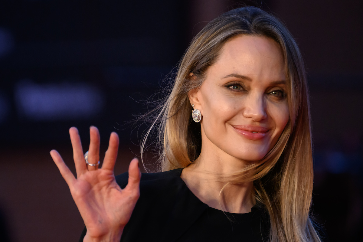 Angelina Jolie fekete felsőben, nagy fülbevalóval integet