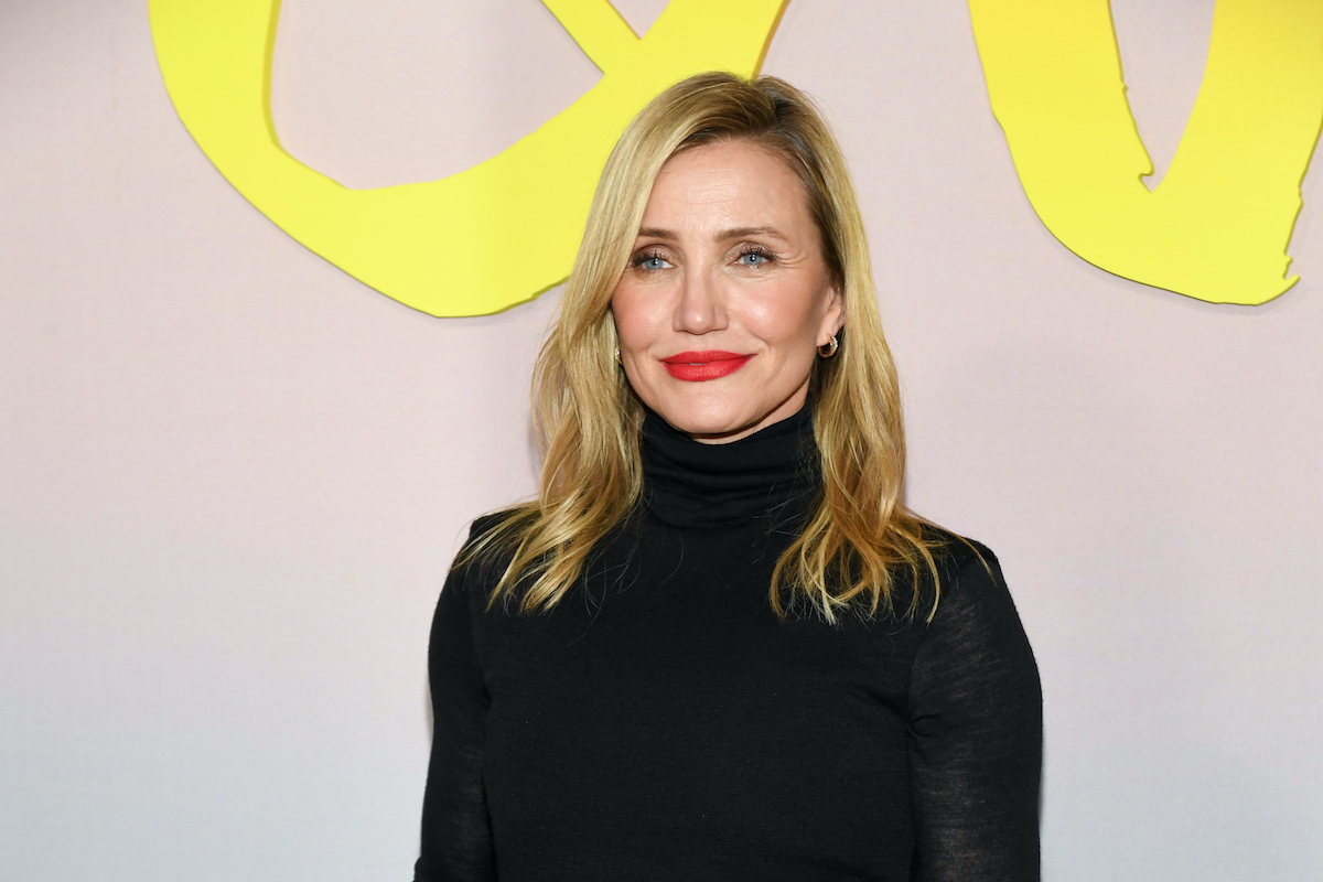Cameron Diaz sárga felirat előtt fekete garbóban és piros rúzzsal
