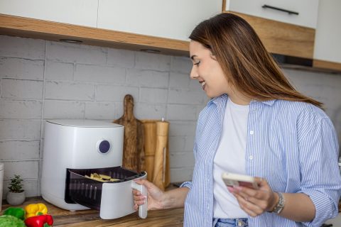 Fiatal nő fehér air fryer fiókját húzza ki konyhában állva.