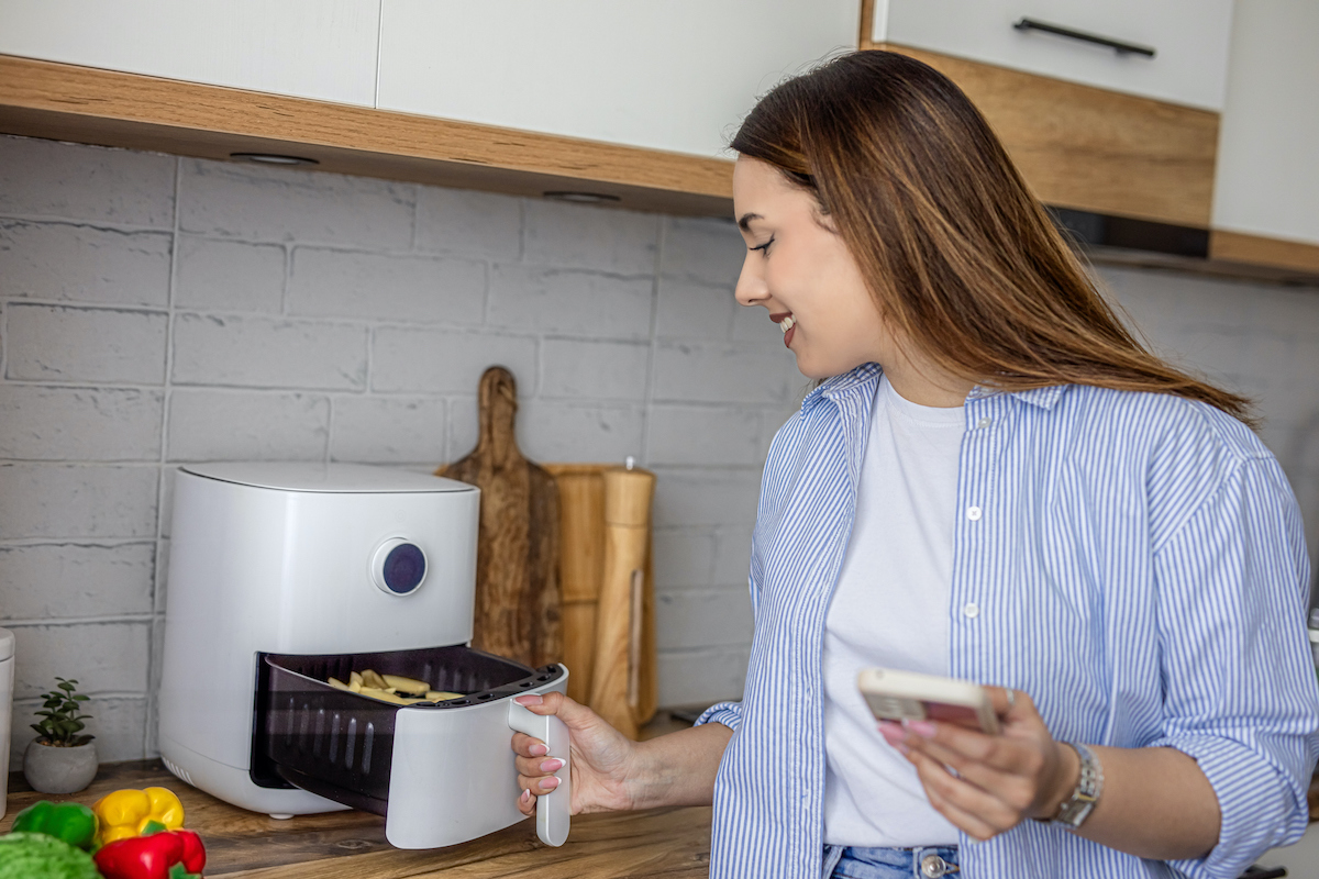 Fiatal nő fehér air fryer fiókját húzza ki konyhában állva.
