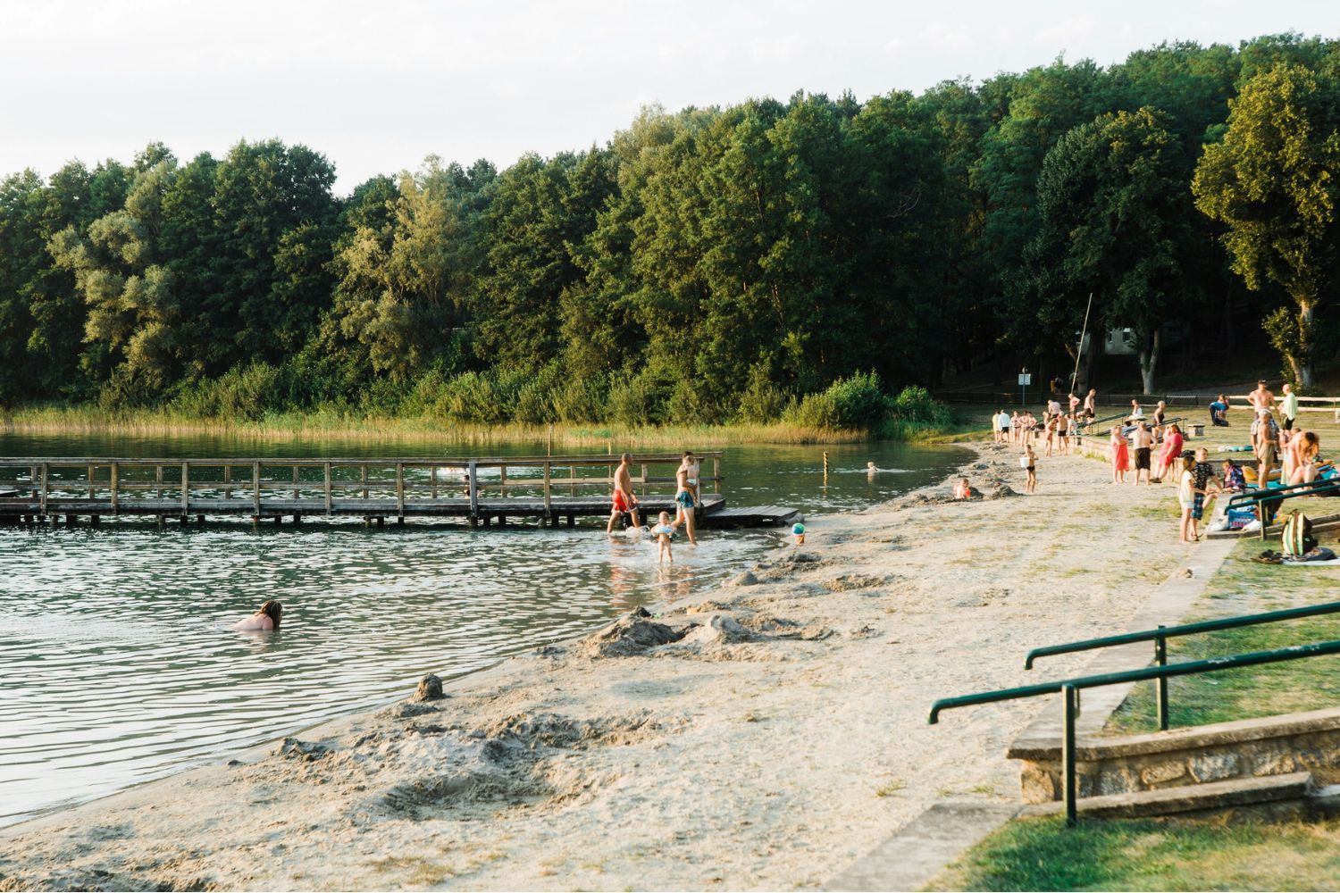 Természetes tóparti strand fa stéggel, strandolókkal