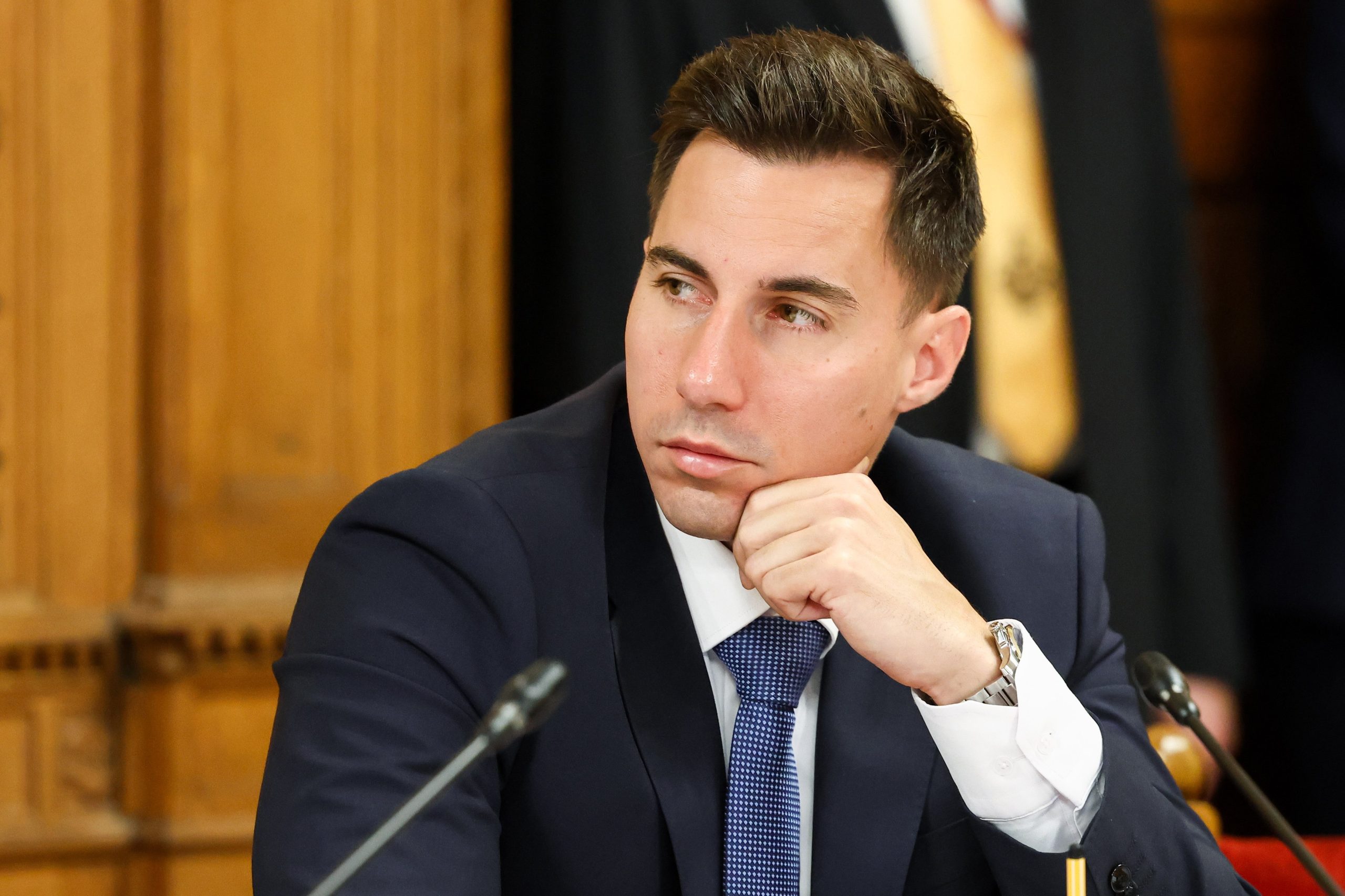 Radnai Márk sötétkék öltönyben és nyakkendőben mikrofon előtt ül