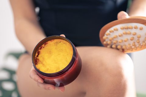 nő krémezi a combját, narancsbőr elleni testradírt és fatüskés masszírozót használ