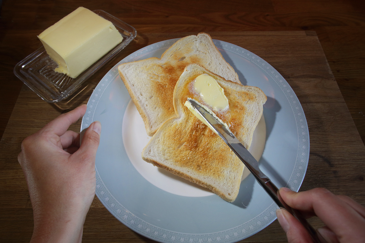 tányéron 2 szelet toast kenyér, női kéz megvajazza