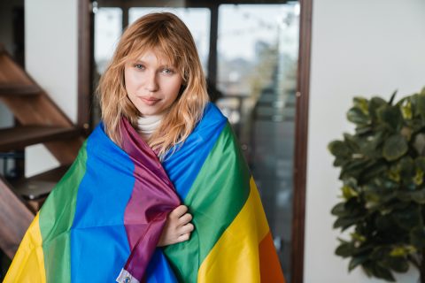 szőke fiatal nő LGBT zászlóba takarva