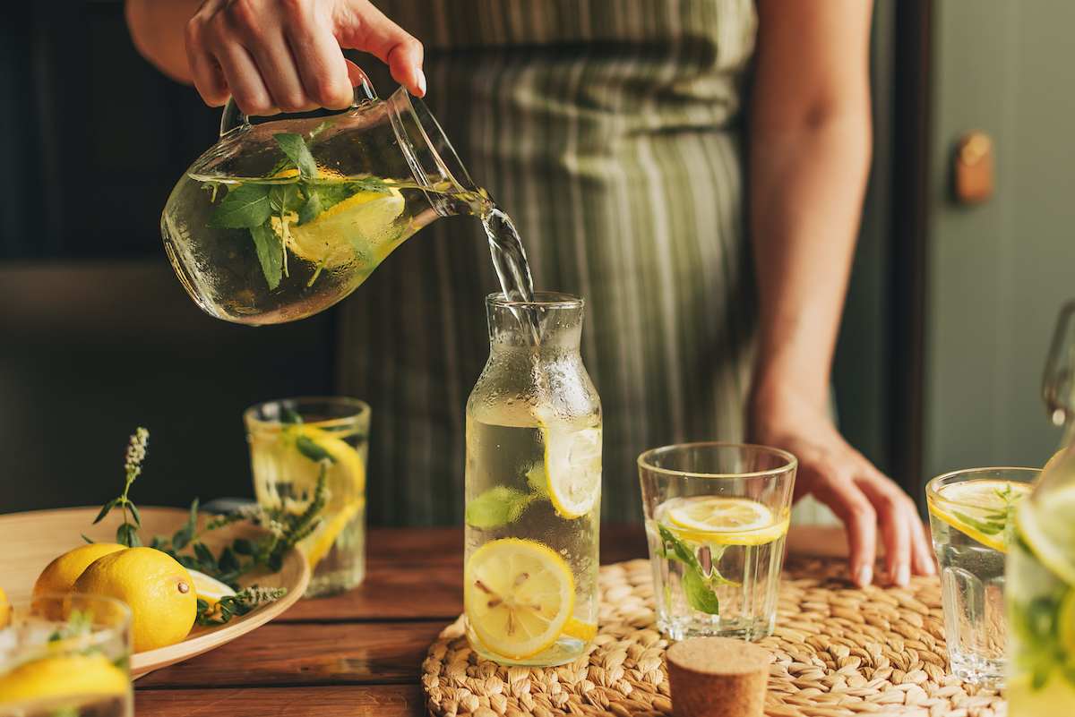nyari-ital-gyumolcsos-vizek | Marie Claire részlet: kézben tartott limonádés kancsó, körülötte poharak és más kiegészítők