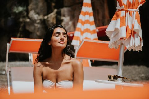 Nyugodt nő mosolyogva élvezi a napsütést a strandon narancssárga napágyakon