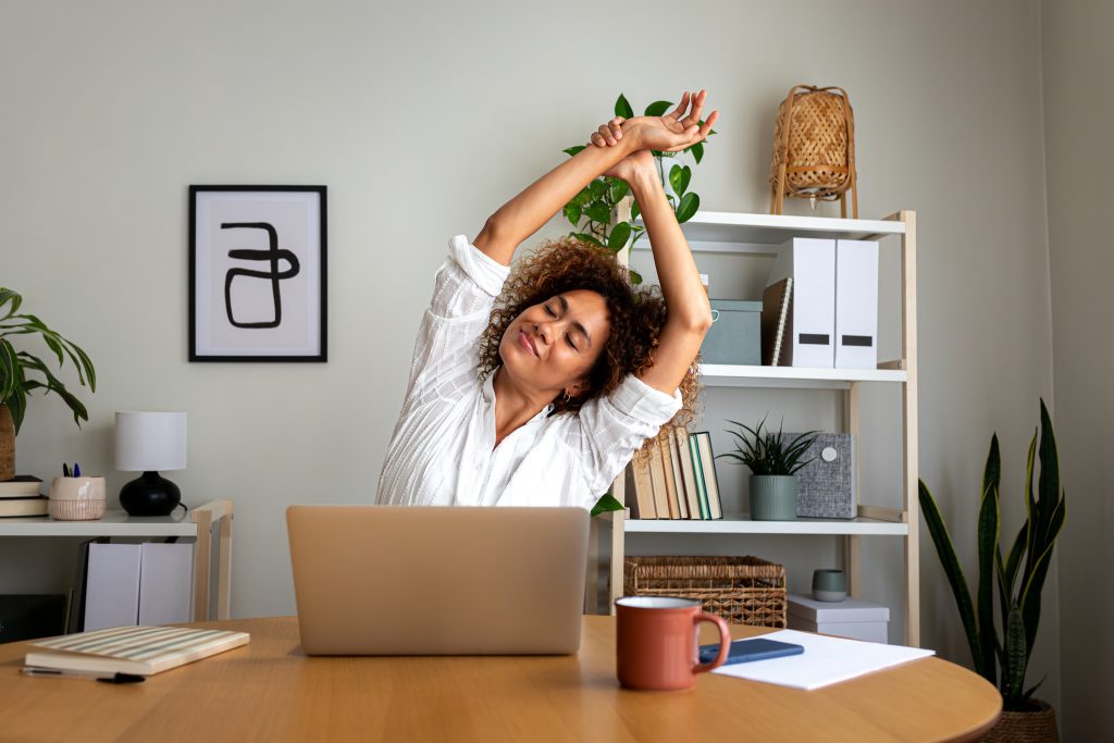 Nő mosolyogva nyújtózkodik a laptopja előtt