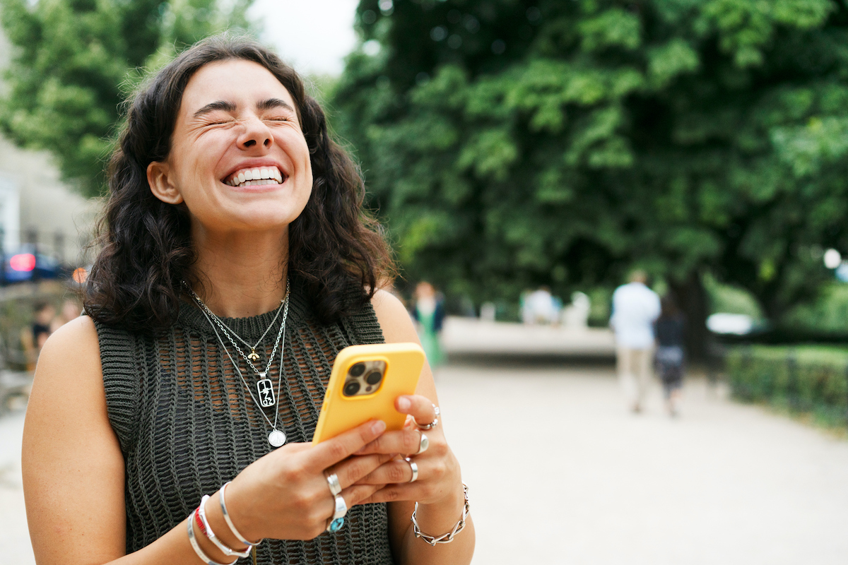 fiatal nő mobiltelefont tart a kezében és behunyt szemmel nevet