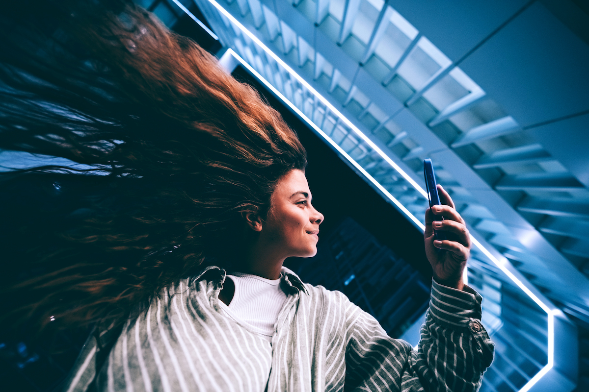 fiatal nő mobiltelefonre néz, felette korlátok, lépcső