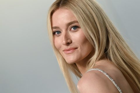 Sarah Pidgeon szőke hajjal hátrafordul, szürke háttér