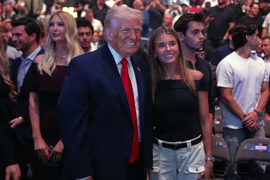 Donald és Kai Trump, Kai fehér rövidnadrágot és fekete felsőt visel, az elnök öltönyben, a háttérben emberek