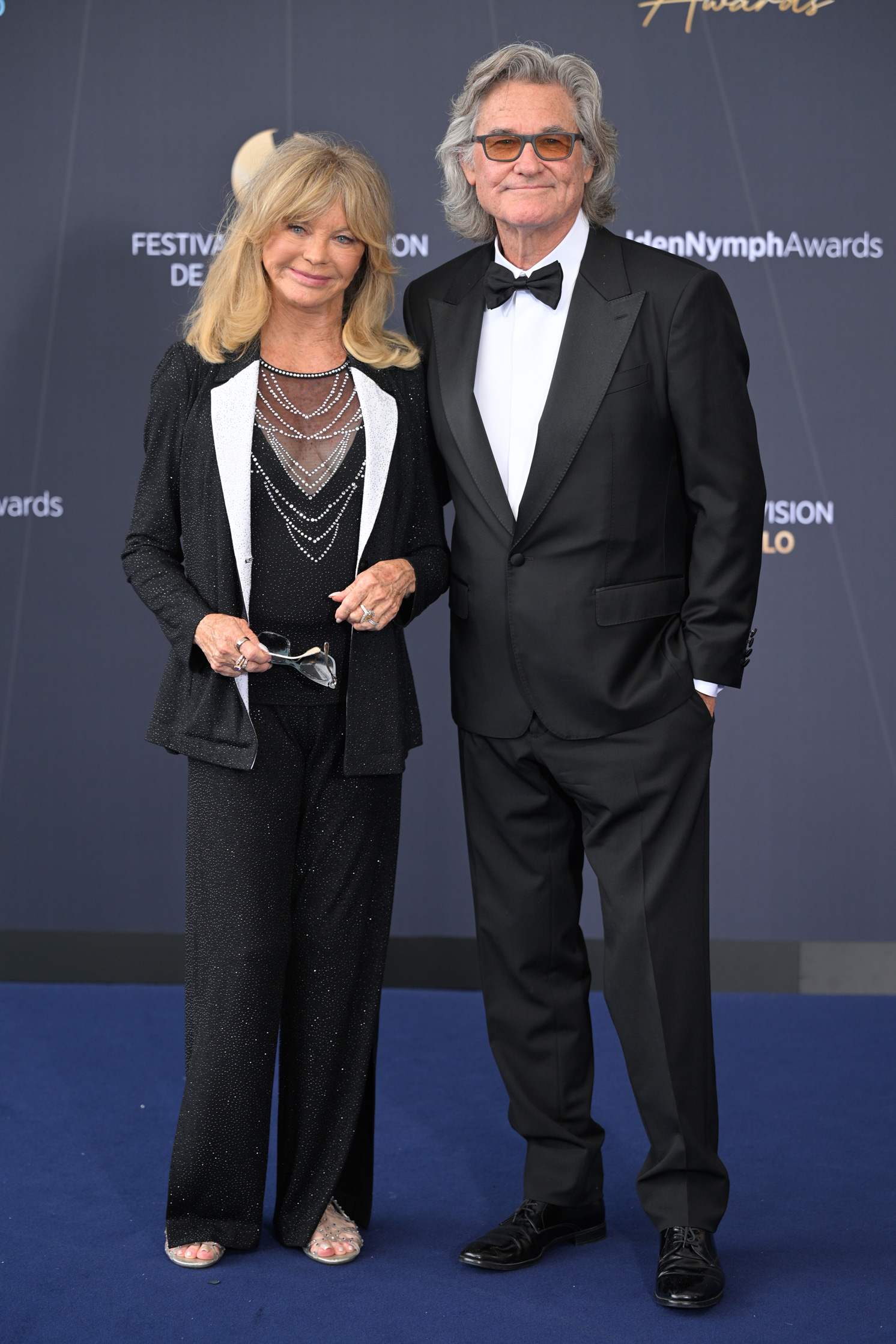 Goldie Hawn és Kurt Russel teljes alakos képe, ahogy visszafogottan mosolyognak a kamerába