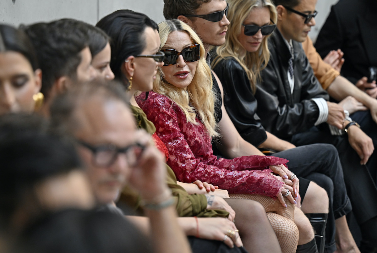 madonna-voros-csipkeruha | Marie Claire Madonna vörös csipkeminiruhában jelent meg a Saint Laurent bemutatóján. A képen napszemüvegben a vendégek között ül.
