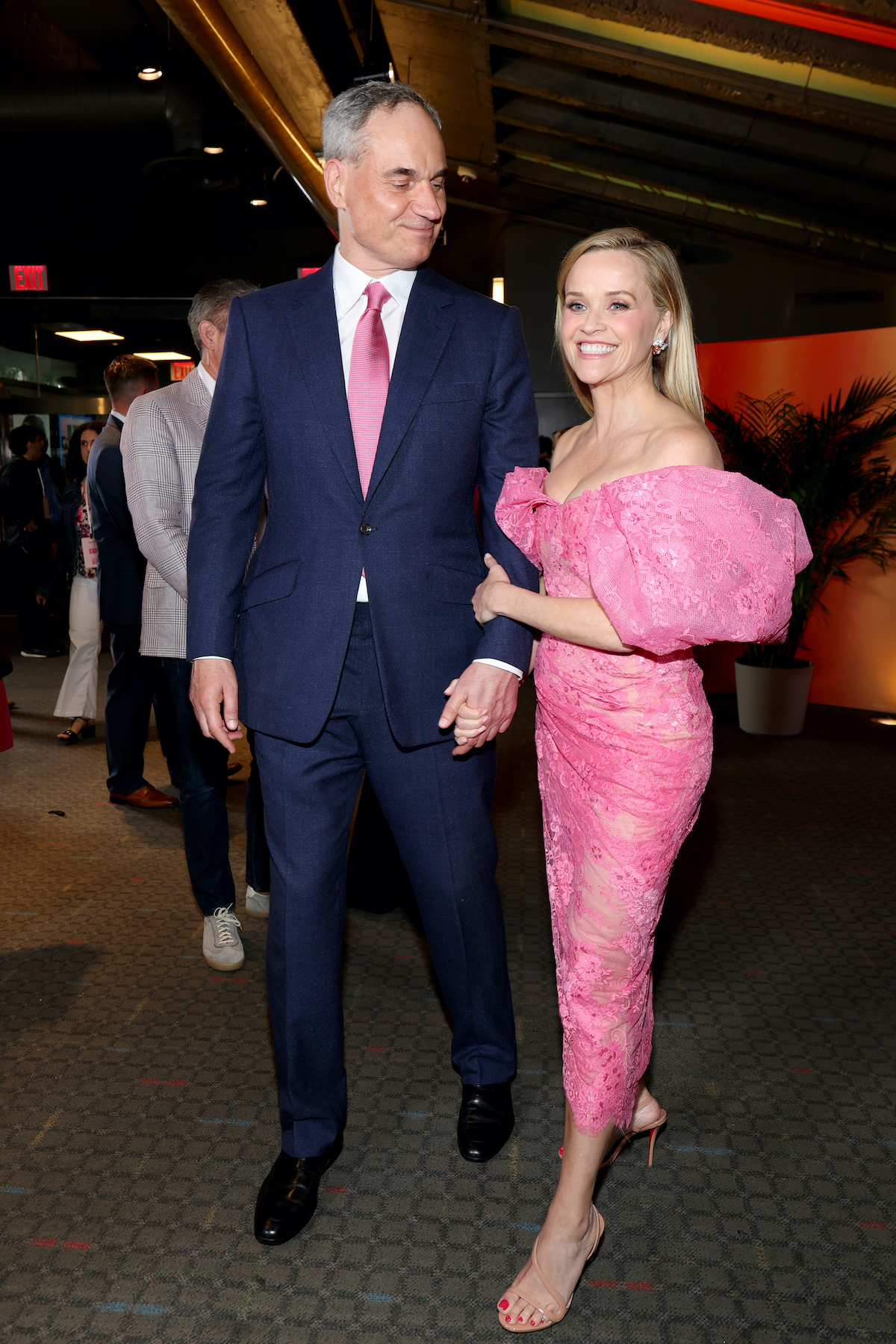 Oliver Haarmann öltönyben és rózsaszín nyakkendőben és Reese Witherspoon rózsaszín ruhában összeölelkezve a kamerába néznek