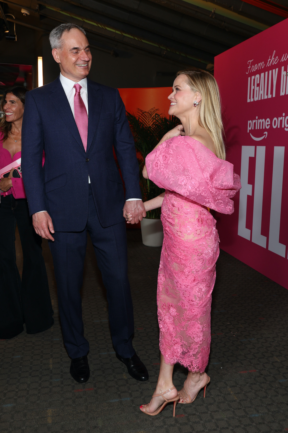 Oliver Haarmann öltönyben és rózsaszín nyakkendőben és Reese Witherspoon rózsaszín ruhában, kéz a kézben egymásra nevetnek