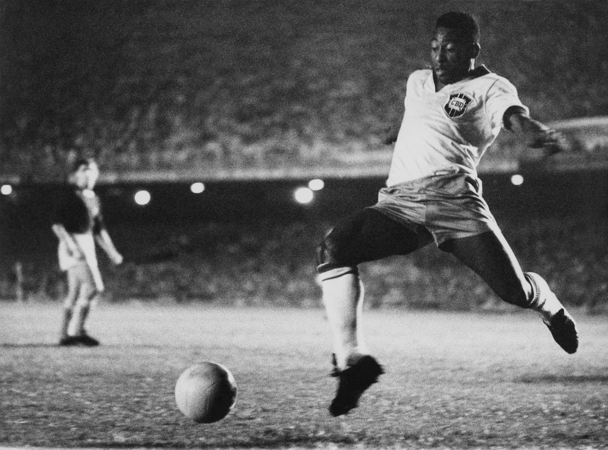 Pele fekete fehér felvételen a pályán labdába rúg épp