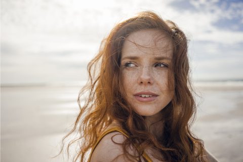 Vörös hajú fiatal nő a strandon - fényvédelem fontossága
