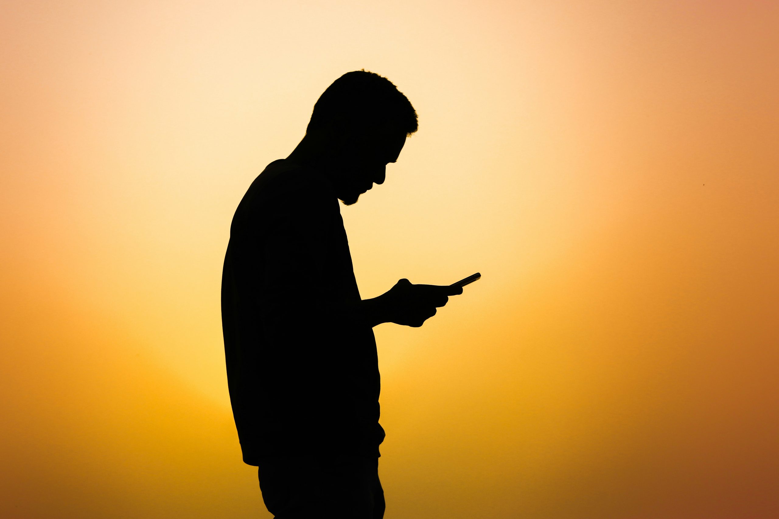 sárga háttér előtt telefonját nyomkodó férfi