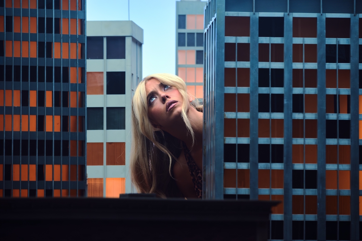 Sydney Sweeney vele egy méretű felhőkarcoló makettek között felfelé néz