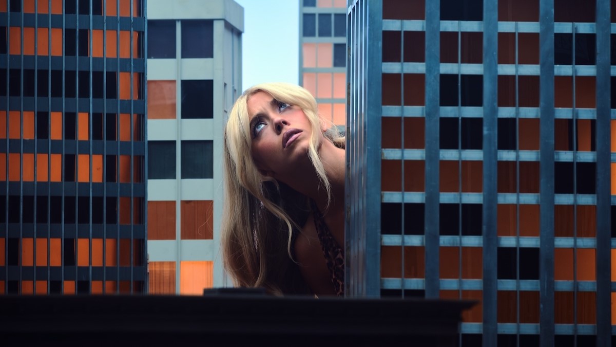 Sydney Sweeney vele egy méretű felhőkarcoló makettek között felfelé néz