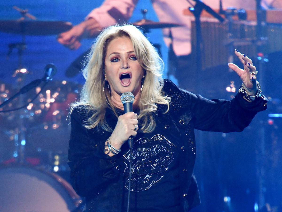 Bonnie Tyler fekete ruhában a színpadon, mikrofonba énekel feltett kézzel