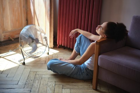Fiatal nő ventillátorral hűsöl a kánikulában