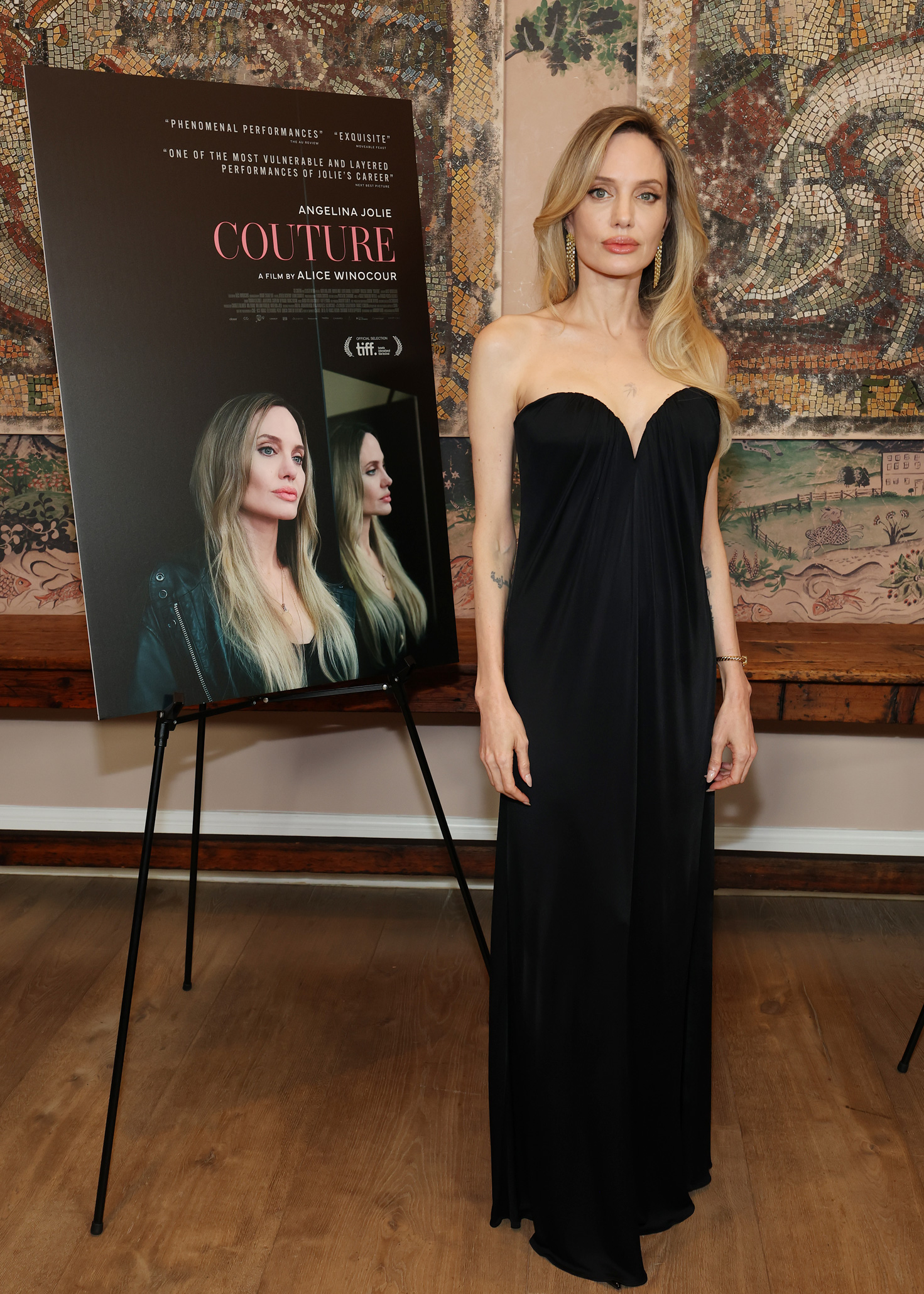 Angelina Jolie teljes alakos képe, amint fekete ruhát visel és komoly arccal néz a Vertical Couture fesztiválon