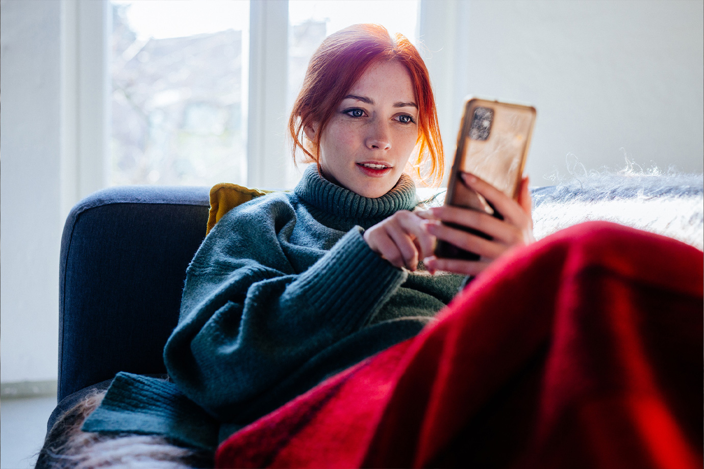 Vörös hajú nő nézi a mobiltelefonja képernyőjét
