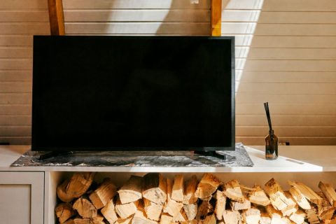 Modern, letisztult fehér fa burolatú lakásban fahasábok tévészekrény aljában, rajta okostévé, alatta alufólialap