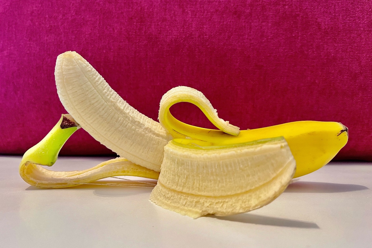 félig meghámozott banán fehér asztalon, magenta színű háttér előtt