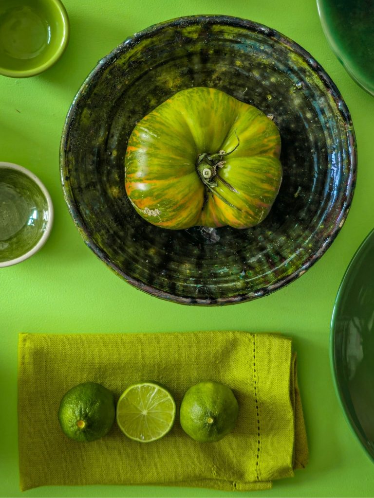 chartreuse-zold-termeszetben | Marie Claire Chartreuse zöld terítő, rajta hasonló árnylatú kerámia edények és egy óriási zöld paradicsom, lime-ok