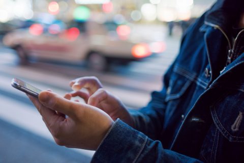 farmerkabátos nő kezében mobiltelefon utcán