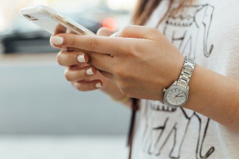manikűrözött női kézben mobiltelefon, a csuklón óra