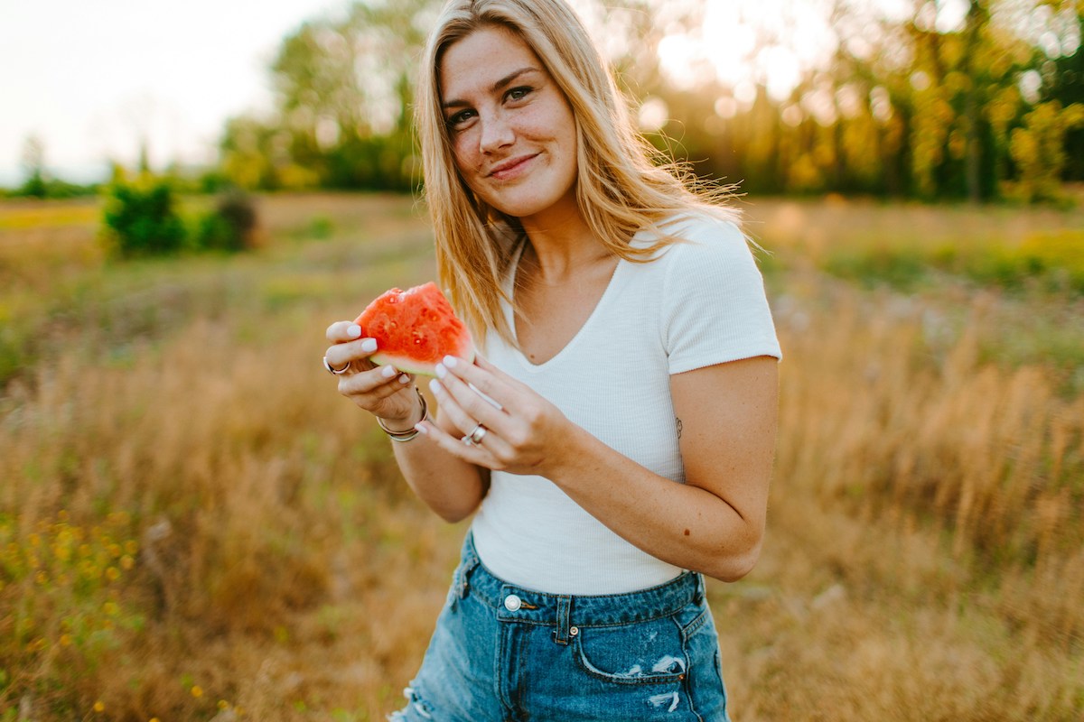 szőke nő természetben, fehér pólóban és farmerben, a kezében görögdinnye