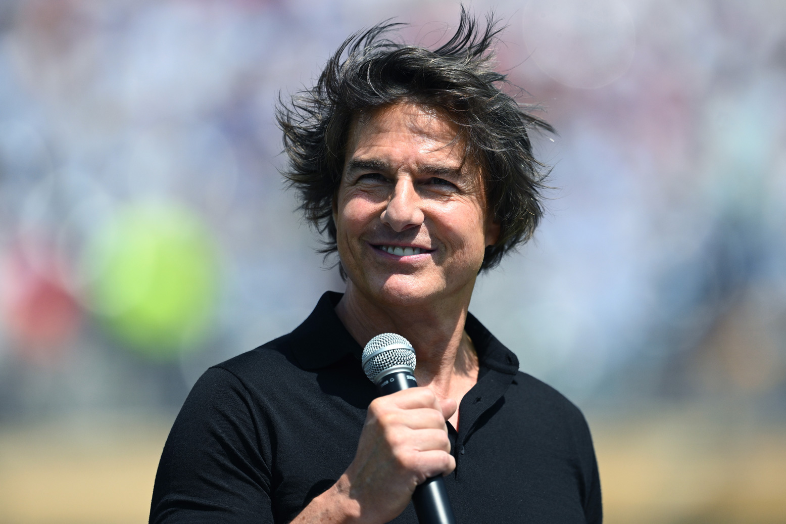 Tom Cruise mikrofonnal a kezében áll és mosolyog