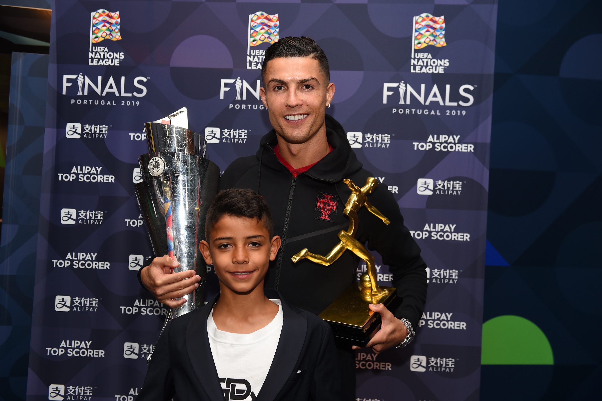 Cristiano Ronaldo portugál válogatott labdarúgó fiával, Cristiano Ronaldo Jr.-ral pózol, miután átvette a torna gólkirályának járó díjat és az UEFA Nemzetek Ligája trófeáját az Portugália–Hollandia UEFA Nemzetek Ligája-döntőt követően a portói Estádio do Dragãóban, 2019. június 9-én