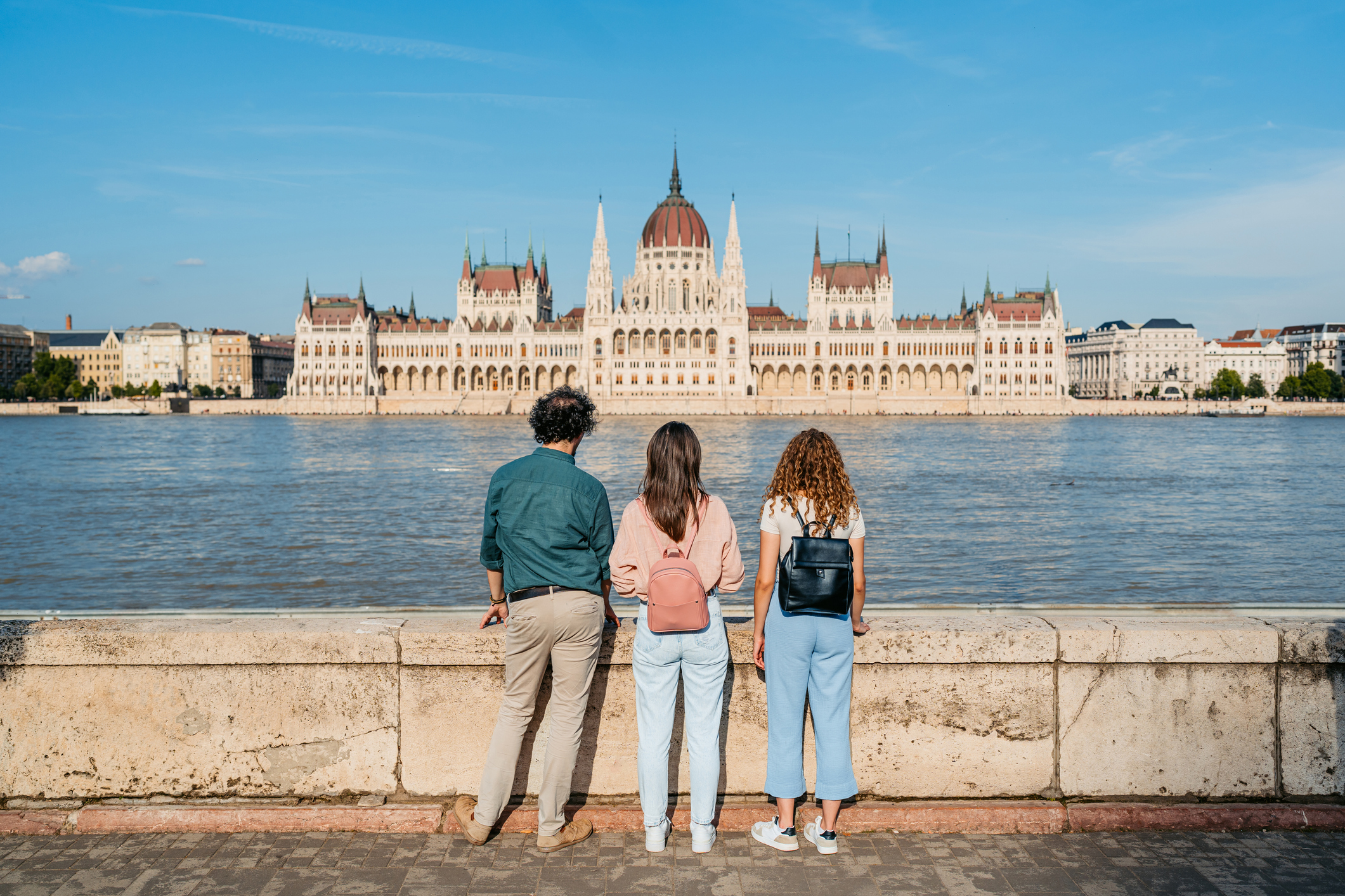 Három barátból álló csoport, akik a Duna túloldalán, a magyarországi Budapest városában a magyar parlament épületére néznek.