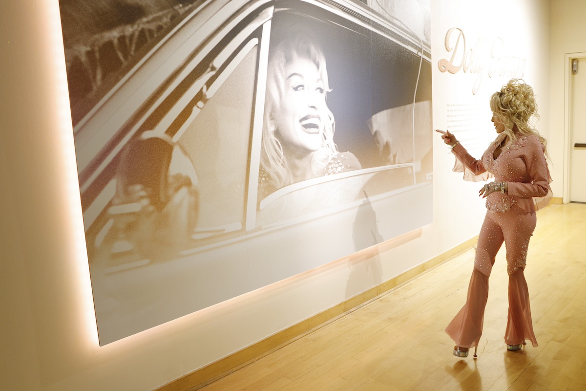Dolly Parton a saját, falra kivetített fényképe előtt áll