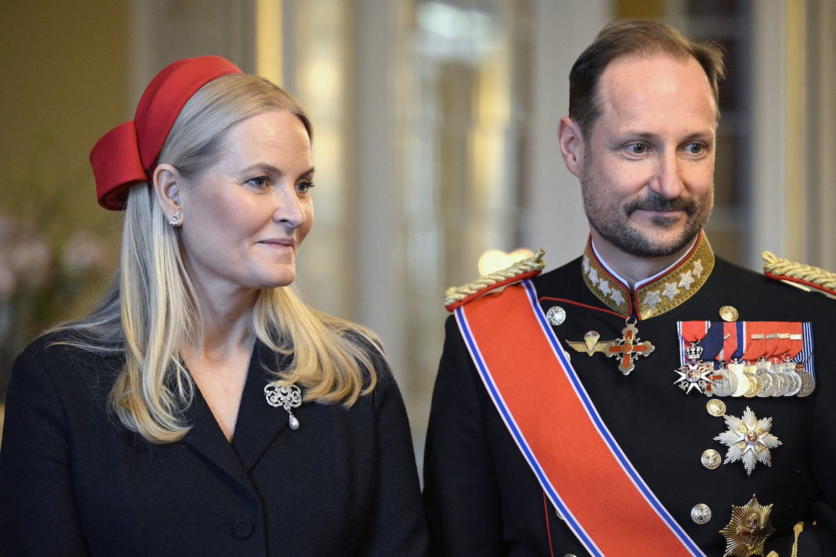 Mette Marit fekete kosztümben és piros kalapban, mellette Haakon