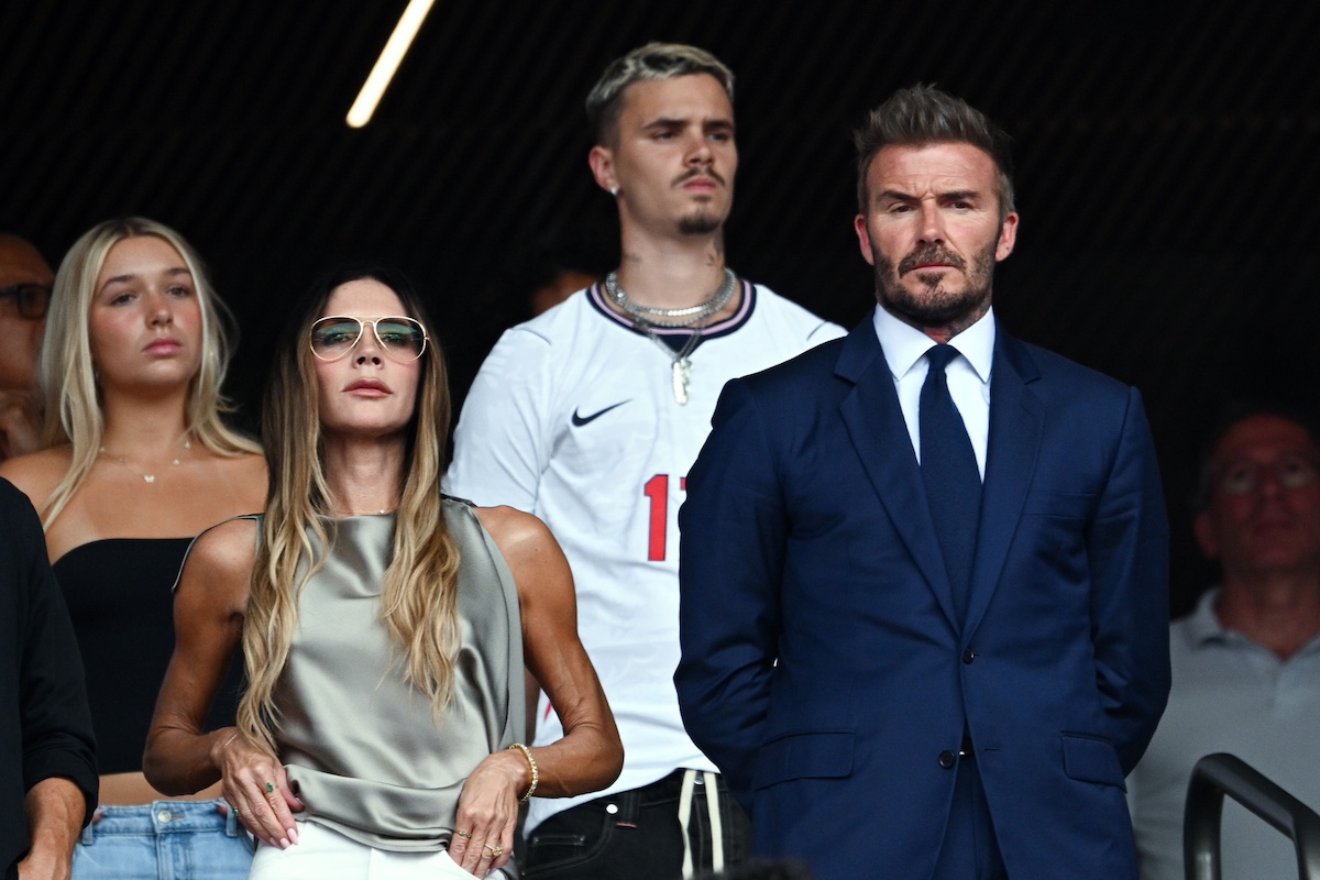 Victoria és David Beckham lelátón, a háttérben fiatal férfi